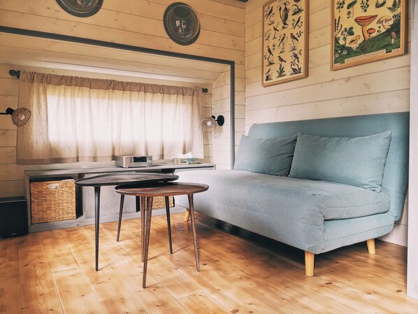 Una habitación acogedora con un sofá, una mesa, una radio y una ventana con cortinas.