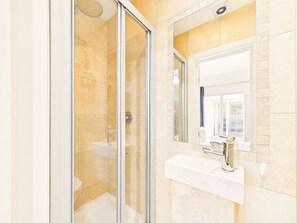 Un bany modern amb una cabina de dutxa de vidre, un lavabo blanc amb un aixeta cromada i un mirall gran sobre el lavabo.