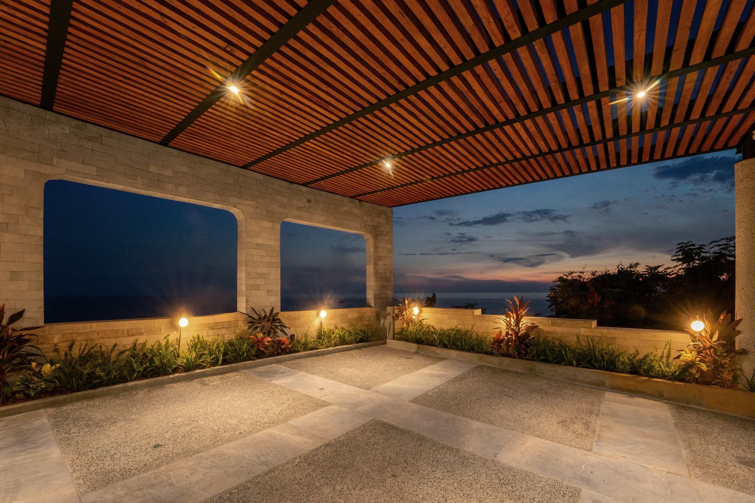 Un espace extérieur aménagé en terrasse, doté d’une pergola, de grandes fenêtres et d’un éclairage décoratif.