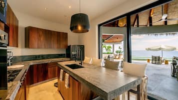 A modern kitchen with a central island, a built-in stove, and a large window overlooking the sea.