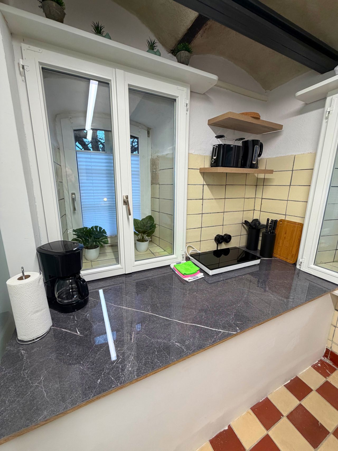 A kitchen with a marble countertop, a coffee maker, a roll of paper towels, and a potted plant.