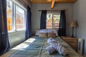 Een slaapkamer met een bed, nachtkastje, lamp en een raam met gordijnen.