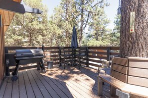 Een houten terras met een barbecue, een tafel met stoelen en een boom.