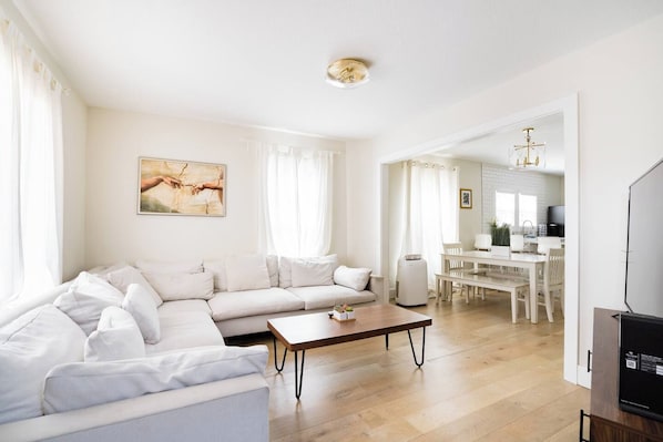 A modern living room with a sofa, coffee table, and a dining area with chairs and a table. - Beds for Ten, Bathrooms for a Family • 4BR (Portland)