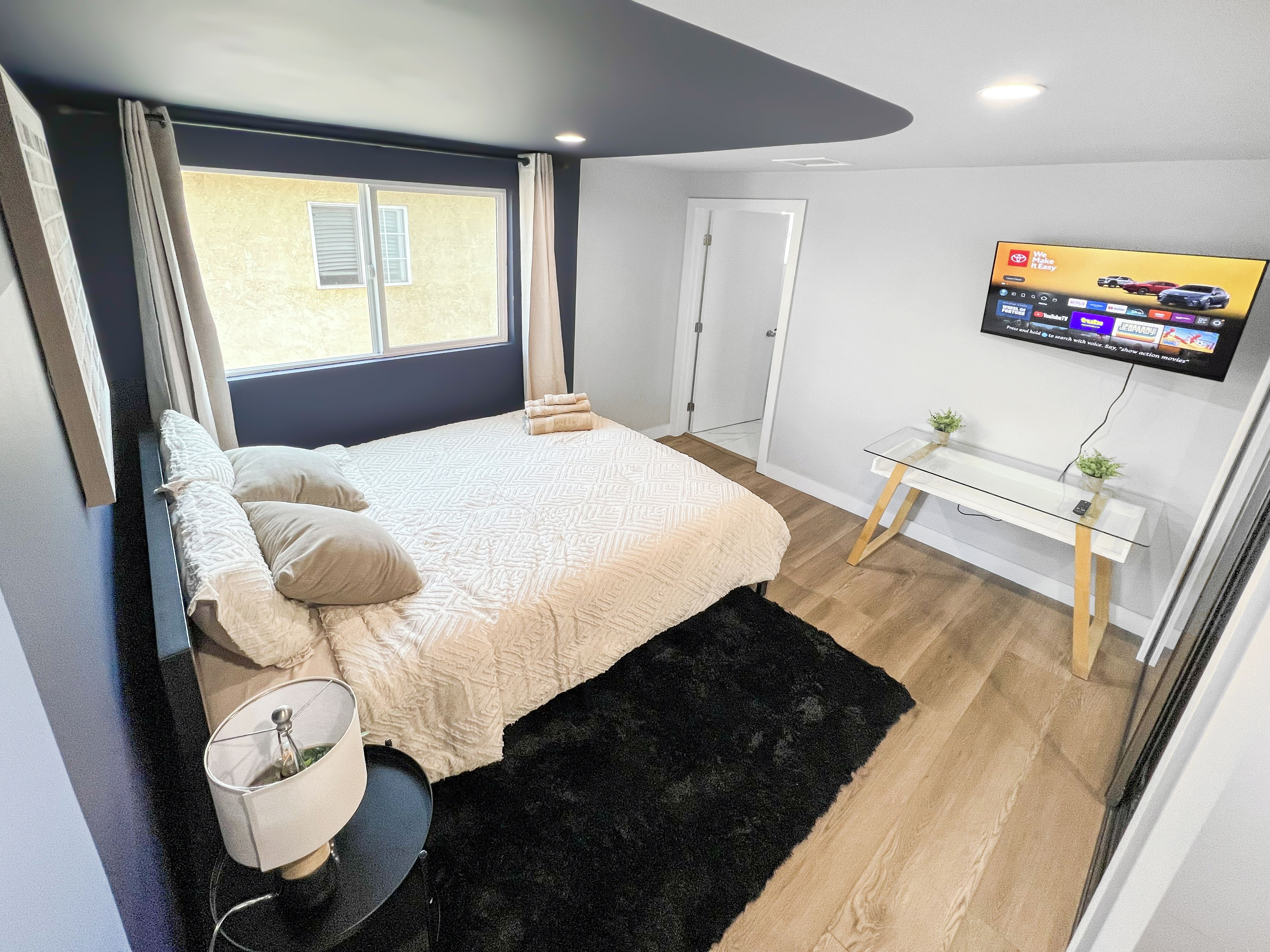A bedroom with a bed, a bedside table, a TV, and a window.