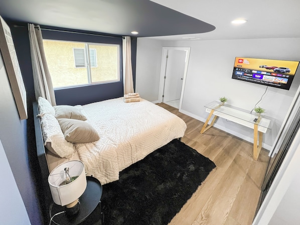 A bedroom with a bed, a bedside table, a TV, and a window. - Bedroom with Private Bathroom (Los Angeles)
