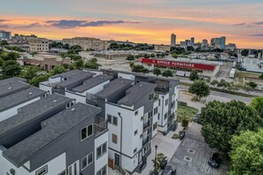 Un immeuble résidentiel à plusieurs étages, doté d’un toit plat, d’une enseigne commerciale indiquant « MOBILIER DE BUREAU », et avec une vue sur les gratte-ciel de la ville en arrière-plan.