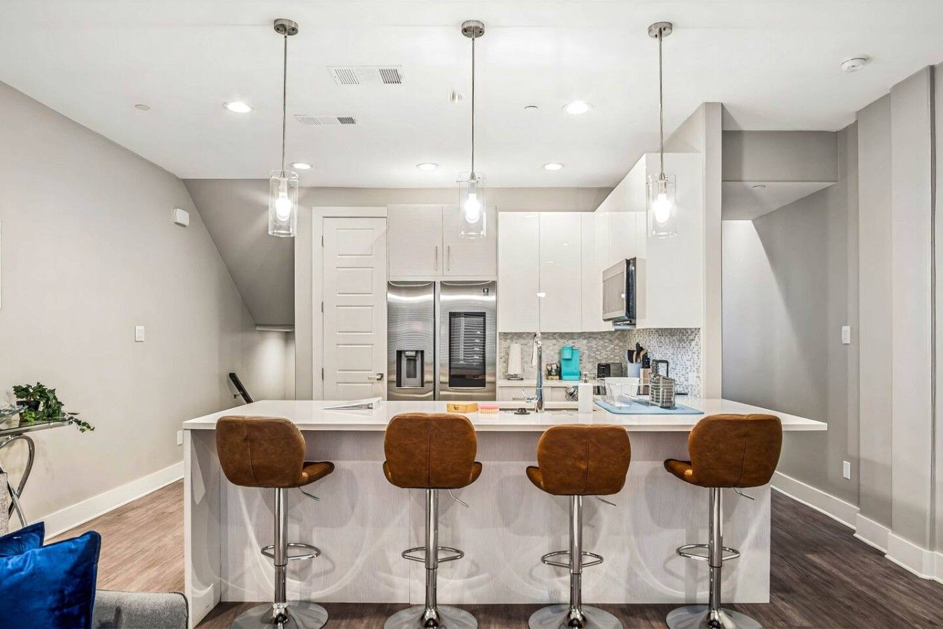 A modern kitchen with a central island, bar stools, stainless steel appliances, and pendant lighting.