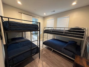 Une chambre avec des lits superposés, une fenêtre avec des stores et un plancher en bois.