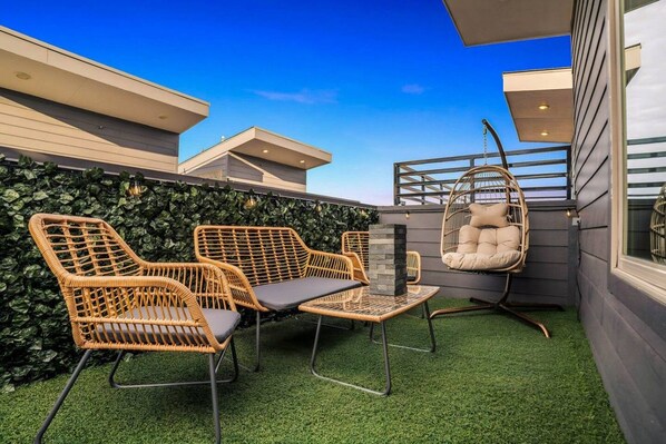 Une terrasse sur le toit, aménagée avec des meubles en osier, un fauteuil suspendu et une petite table.
