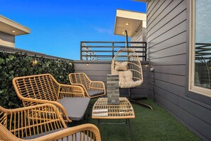 A rooftop patio with wicker furniture, a hanging chair, and a small table. - The Urban Vista Suite *Roof Top Patio Fun!* (Fort Worth)