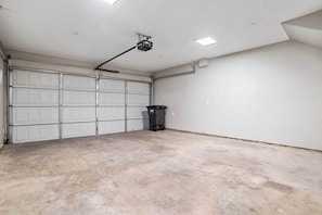 A garage with a white garage door, a projector mounted on the ceiling, and a trash bin on the floor. - The Urban Vista Suite *Roof Top Patio Fun!* (Fort Worth)