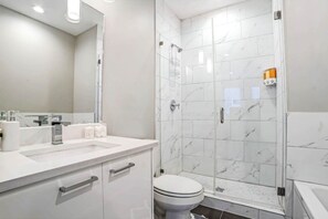 Une salle de bain moderne avec une douche à parois de verre, un lavabo blanc avec un miroir et des toilettes.