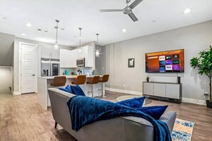 Un salon moderne avec un canapé gris, des coussins bleus, une table basse et un téléviseur fixé au mur.