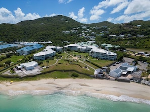 A coastal resort with multiple buildings, a beach, and a mountainous backdrop. - New Listing (anse marcel)