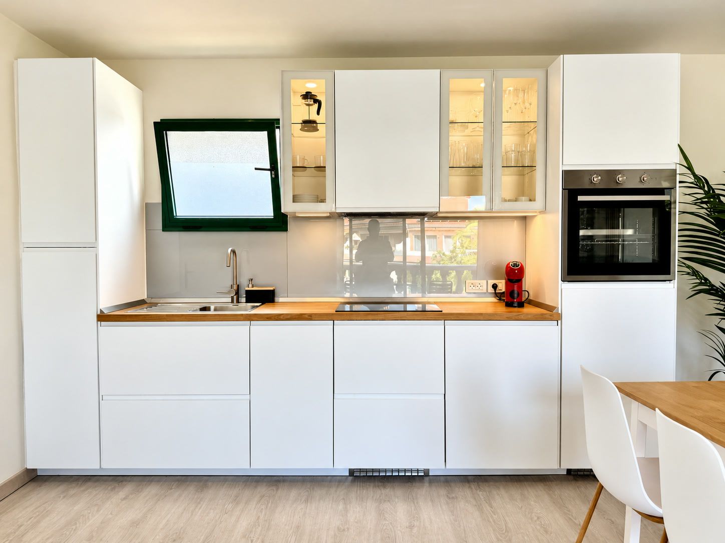 A modern kitchen with white cabinetry, a built-in oven, and a window above the sink.