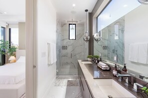 A modern bathroom with a glass shower enclosure, a large mirror, and a vanity with a sink and towel rack. - Luxurious Westside Townhome with Views and Parking (Los Angeles)