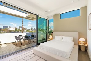 A modern bedroom with a large bed, a balcony with a table and chairs, and a city view. - Luxurious Westside Townhome with Views and Parking (Los Angeles)