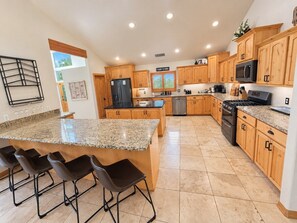 A modern kitchen with granite countertops, wooden cabinets, a central island with bar stools, and stainless steel appliances. - Mountain Meadow Ranch Private 5-Acre Escape (Parks)