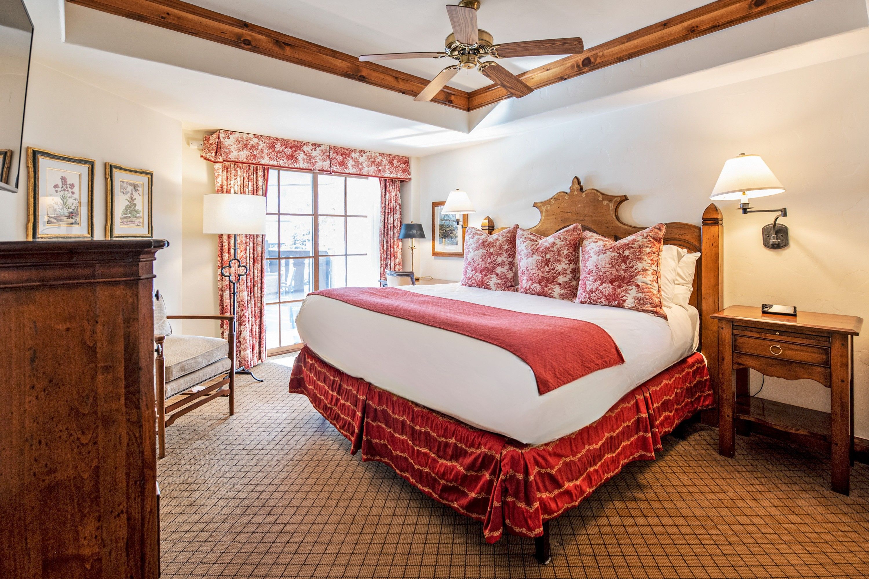 A bedroom with a large bed, wooden headboard, two bedside lamps, a wooden nightstand, a chair, and a window with curtains.