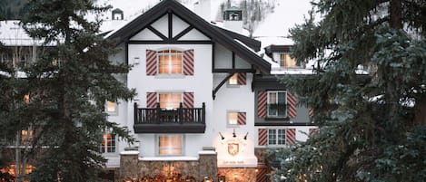 Ett hotell med en traditionell europeisk arkitektur, kännetecknat av en framträdande entré med en glasdörr och en balkong.