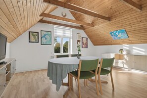 A dining area with a round table, green chairs, and a window with a view of trees.