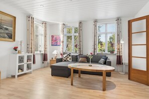 A living room with a sofa, a coffee table, a cabinet with decorative items, and large windows with curtains.