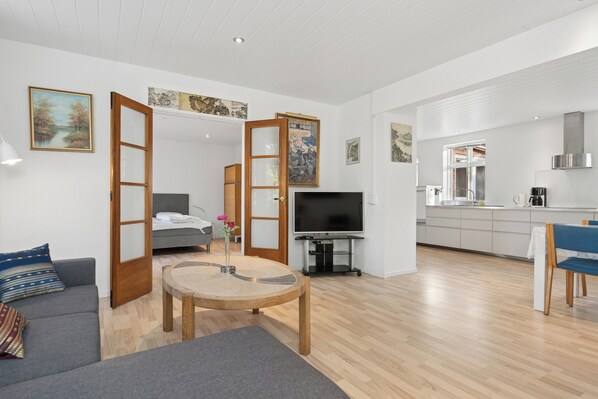 A modern living space with a sofa, a round table, a television, and a kitchen area.