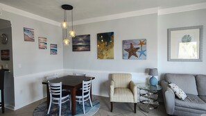 Un comedor con una mesa redonda y sillas, una zona de estar con un sofá y sillón, y decoración en la pared que incluye una pintura de una estrella de mar.