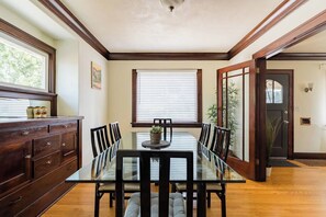 A dining area with a glass table, wooden chairs, a dark wooden cabinet, and a window with blinds.
