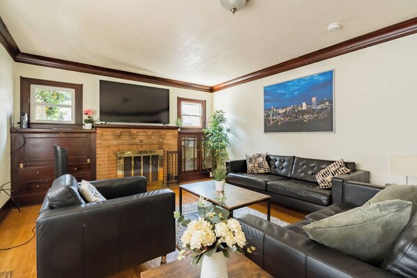 A living room with a fireplace, leather sofas, a flat-screen TV, and a cityscape painting.