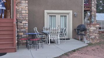 An outdoor patio with a table and chairs, a barbecue grill, and a stone wall.