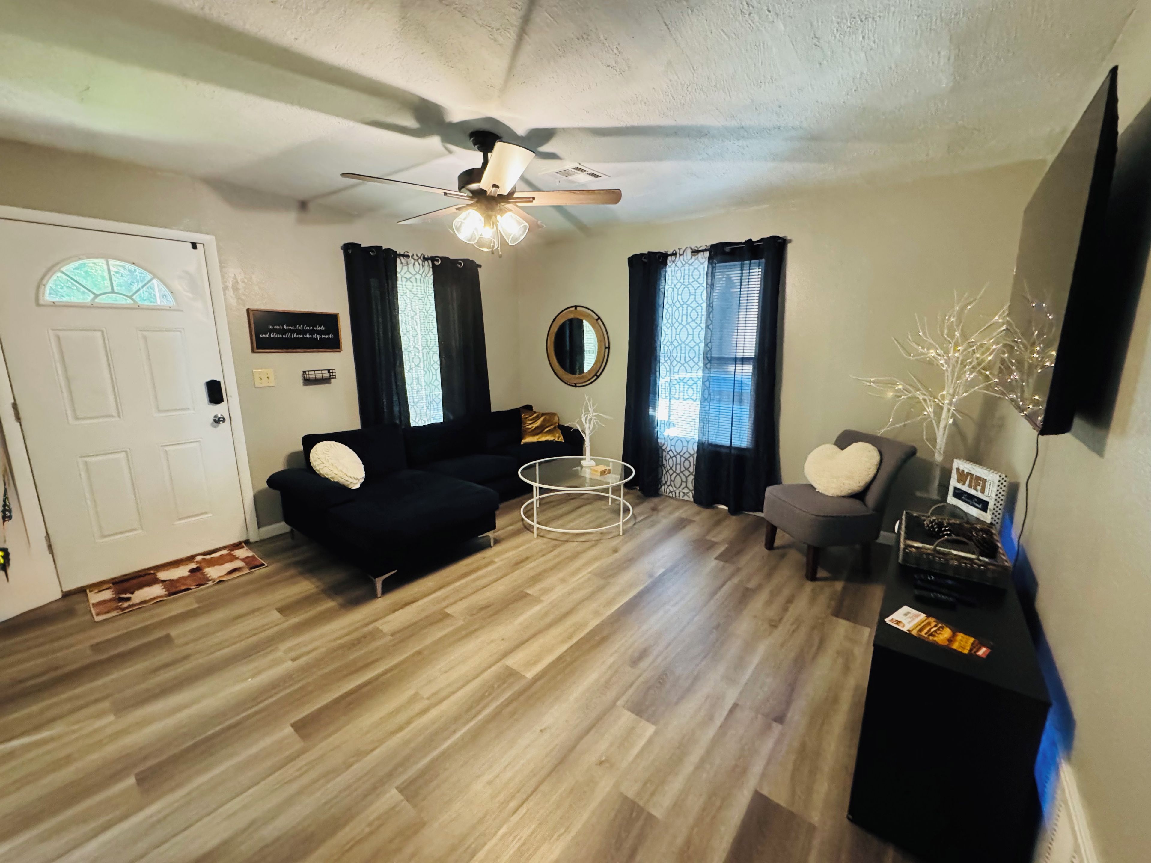A living room with a ceiling fan, a black sofa, a round coffee table, and a grey armchair.