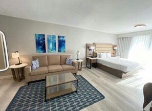 Una habitación de hotel con cama, sofá, mesa de centro y obras de arte en la pared.