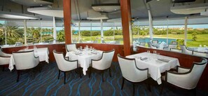Un restaurante con mesas dispuestas para comer, ventanas amplias que dan a un campo de golf y una piscina.
