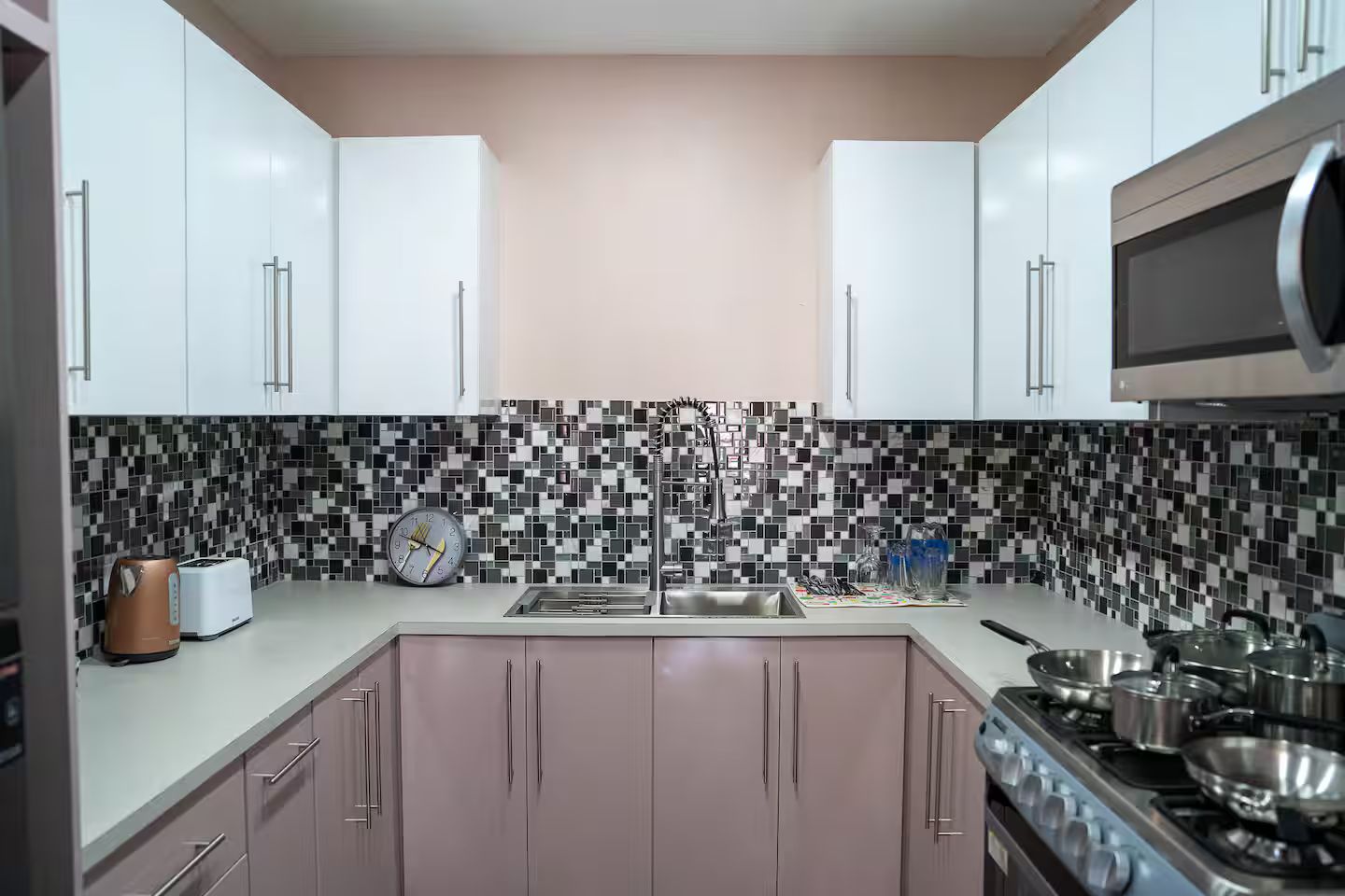 A modern kitchen with white cabinets, a black and white mosaic backsplash, a stainless steel sink, and a gas stove.