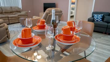Ein Esstisch, gedeckt mit orangefarbenem Geschirr und Weingläsern, umgeben von Sofas und einem Fernseher in einem Wohnzimmer.