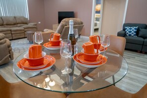 A dining table set with orange tableware and wine glasses, surrounded by sofas and a television in a living room. - Gulf Residence Apt4 (La Romaine)