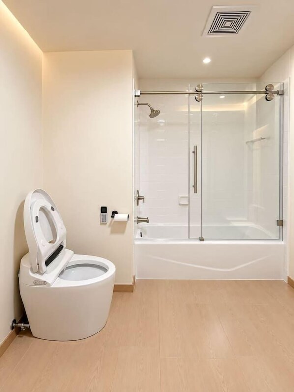 Et moderne badeværelse med toilet, glasvæg omkring brusebad og badekar.