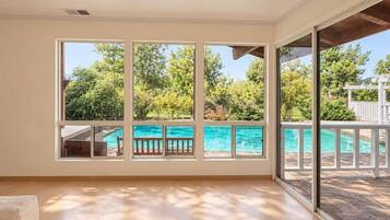 A spacious room with large windows overlooking a swimming pool and lush greenery.