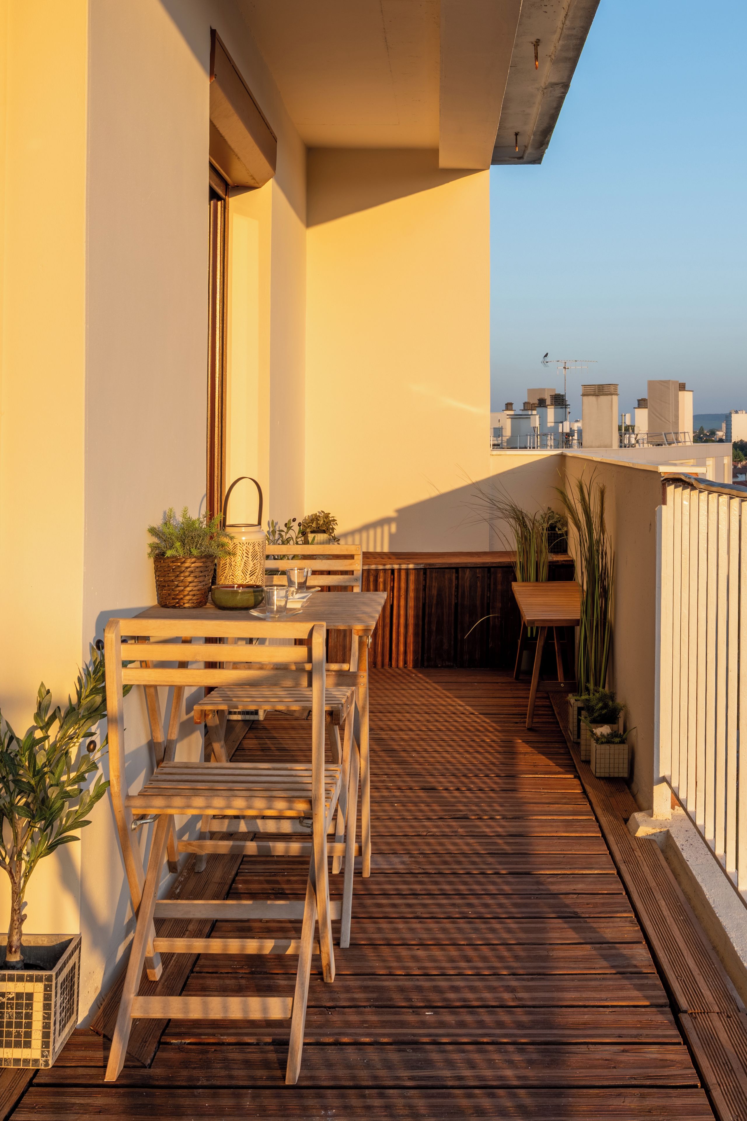 A wooden deck with a table and chairs, potted plants, and a view of the cityscape.