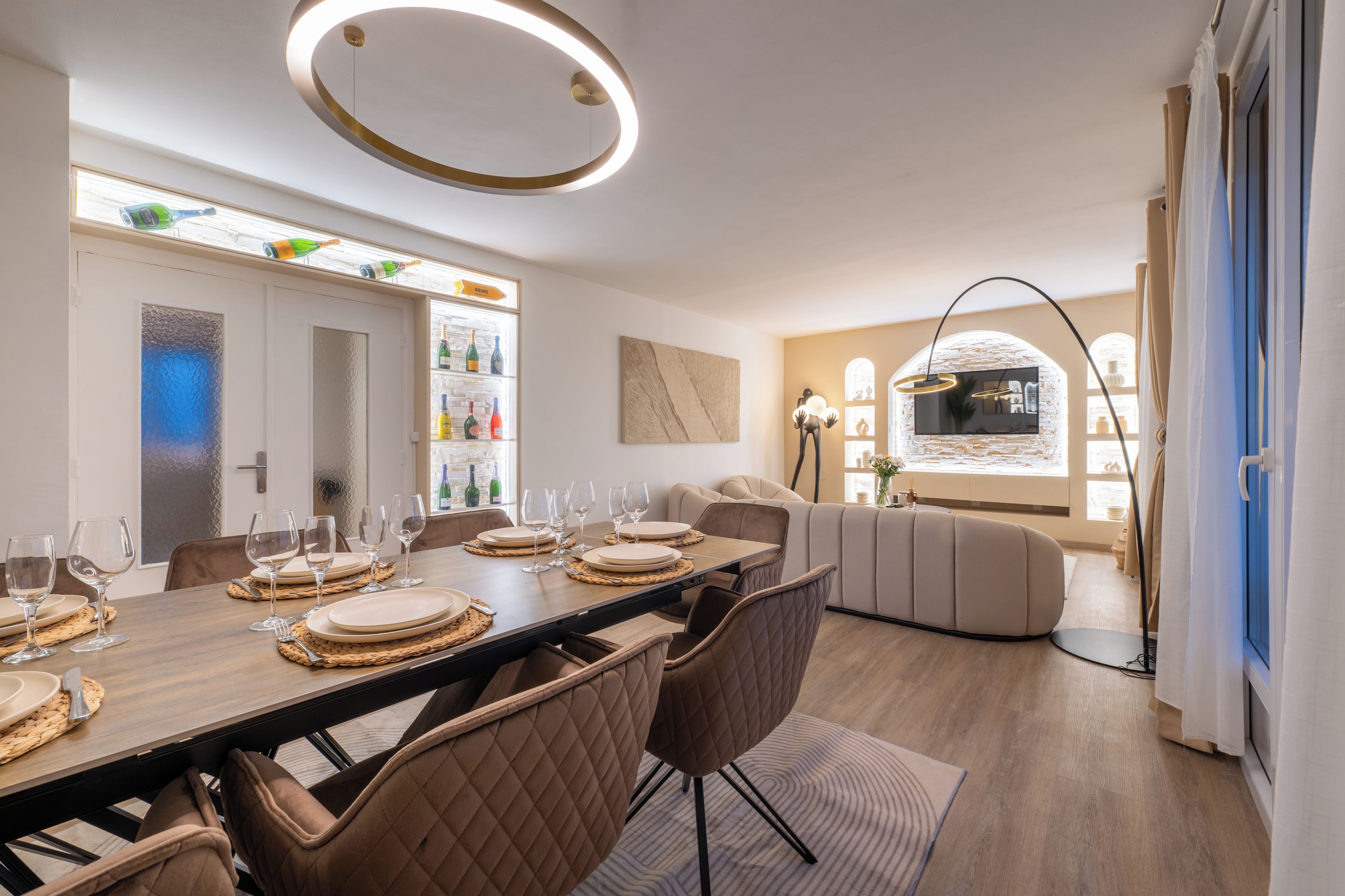 Un espace de repas moderne avec une longue table dressée pour six personnes, un canapé et un téléviseur en arrière-plan.