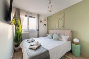 A neatly arranged bedroom with a bed, pillows, a bedside table, a plant, and a window with curtains. - New Listing (Tinqueux)