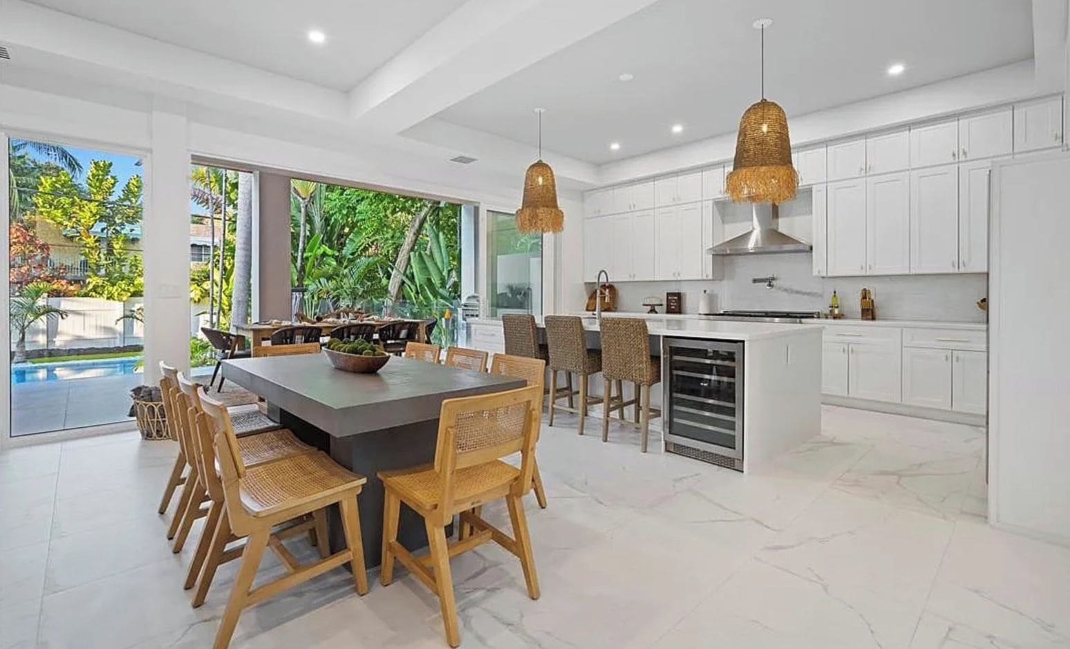 Una cocina moderna con armarios blancos, una isla central y una zona de comedor con sillas de mimbre.