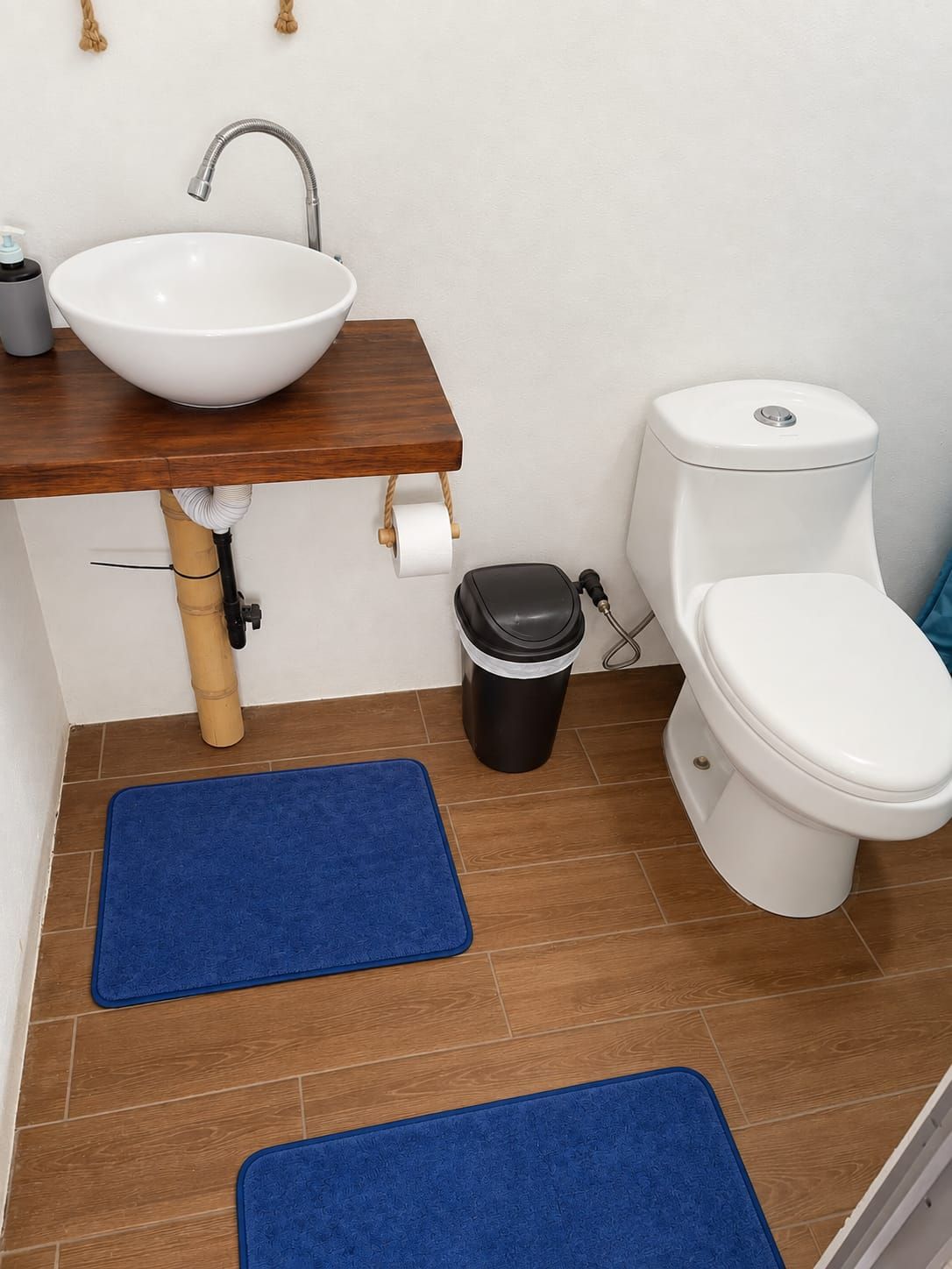 Un baño con lavamanos blanco, encimera de madera, inodoro y dos felpudos azules en el suelo.