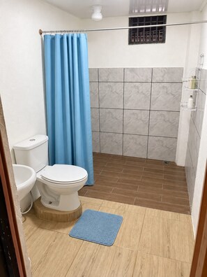 Un baño con inodoro, ducha con cortina azul y pared de ducha con azulejos.