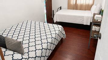 A bedroom with two beds, a wooden floor, a door, and a small shelf with toiletries.