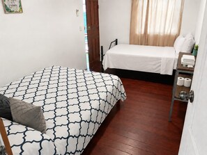 Un dormitorio con dos camas, piso de madera, una puerta y un pequeño estante con artículos de aseo.