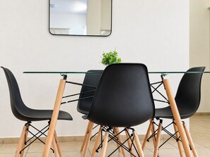 A modern dining area with a glass table and black chairs with wooden legs. - Cerritos Housing (La Paz)