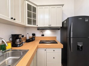 A compact kitchen with white cabinets, a black refrigerator, a coffee maker, and a built-in stove. - Cerritos Housing (La Paz)